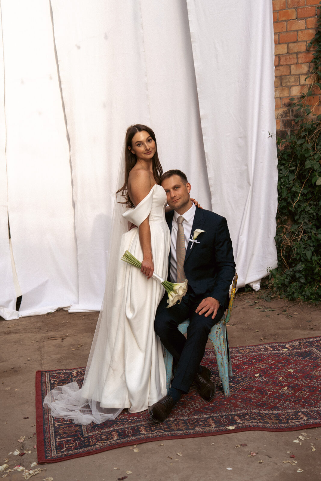 Bride and groom seated together in front of a white curtain