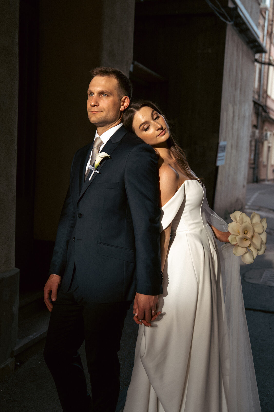 Bride and groom standing back to back in dramatic light