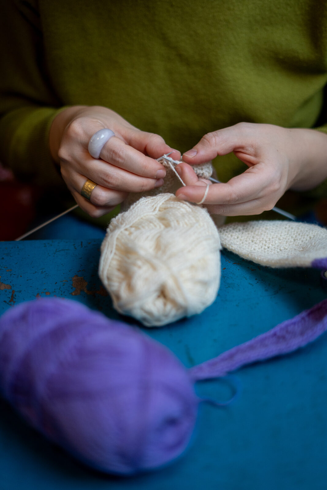 Hands knitting with cream wool at a table
