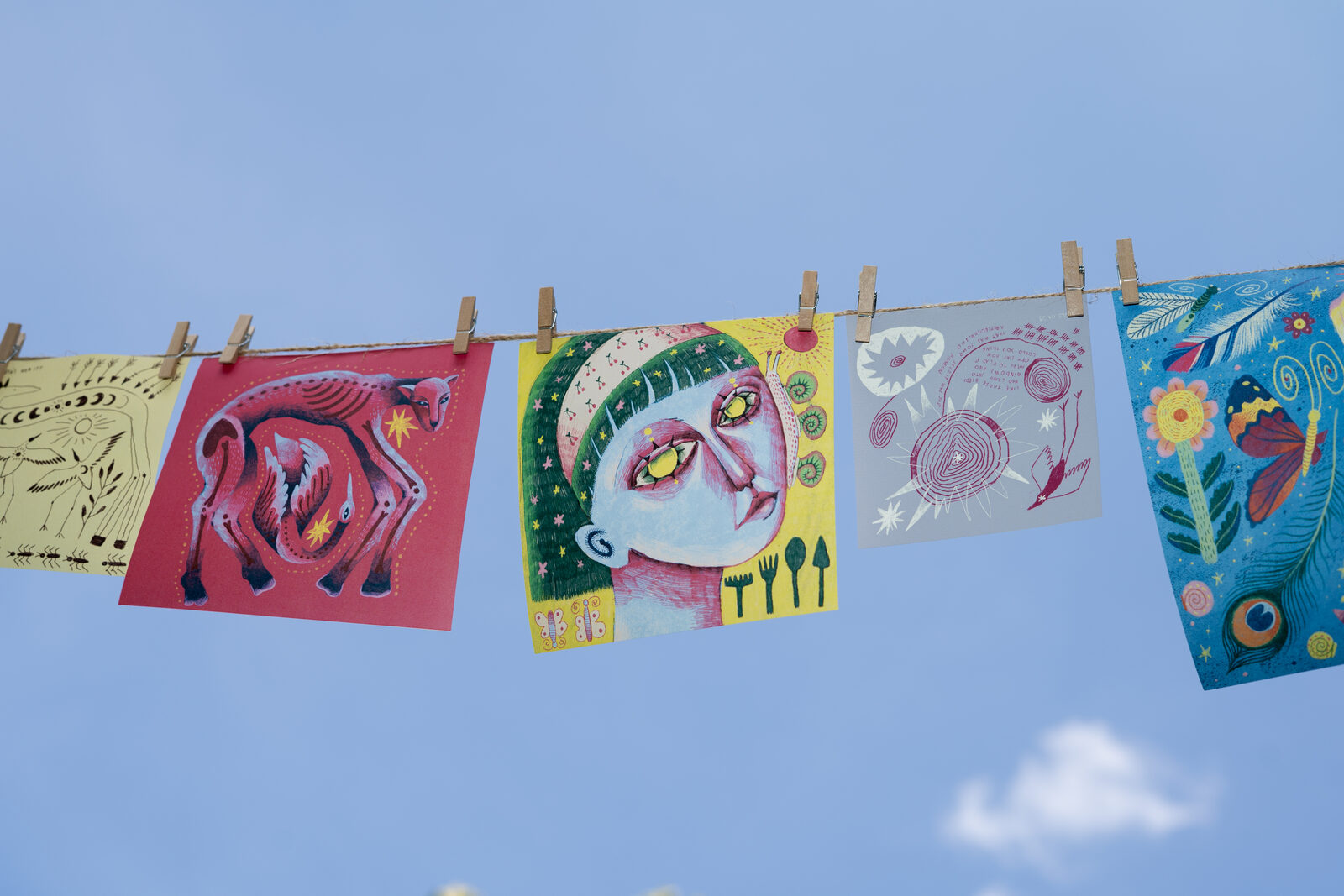 Illustrated postcards pegged to a line against a blue sky